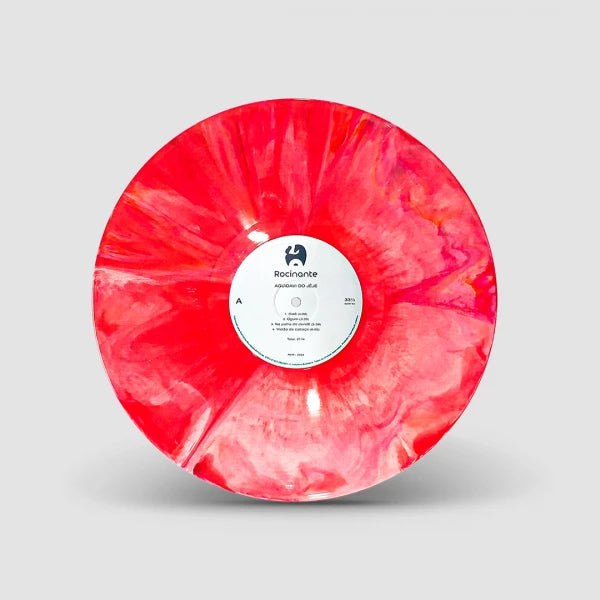 Disco de vinil vermelho marmorizado do álbum “Aguidavi do Jeje” do grupo Aguidavi do Jeje, com mesclas em tons de vermelho, rosa e laranja e rótulo central branco da Rocinante, isolado sobre fundo neutro (disco de vinil).