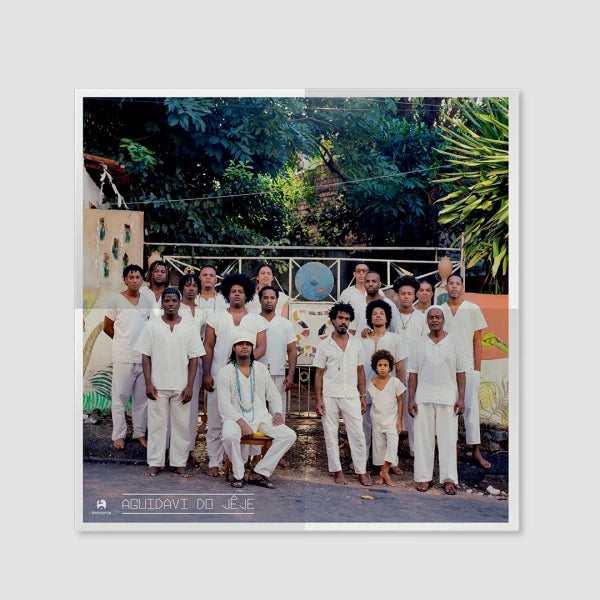 Pôster do álbum “Aguidavi do Jeje” do grupo Aguidavi do Jeje em formato disco de vinil, com fotografia do grupo vestido de branco reunido em área externa arborizada, com elementos de percussão e logotipo da Rocinante no canto inferior direito (disco de vinil).