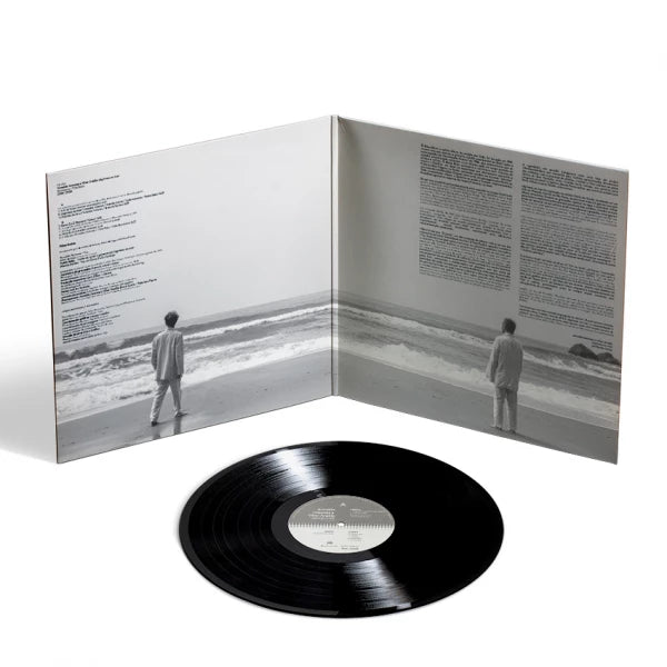 Capa gatefold aberta do álbum “Lágrimas no Mar” de Arnaldo Antunes e Vitor Araújo em disco de vinil, com fotografias em preto e branco da praia, textos impressos nas páginas internas e disco preto posicionado à frente (disco de vinil).