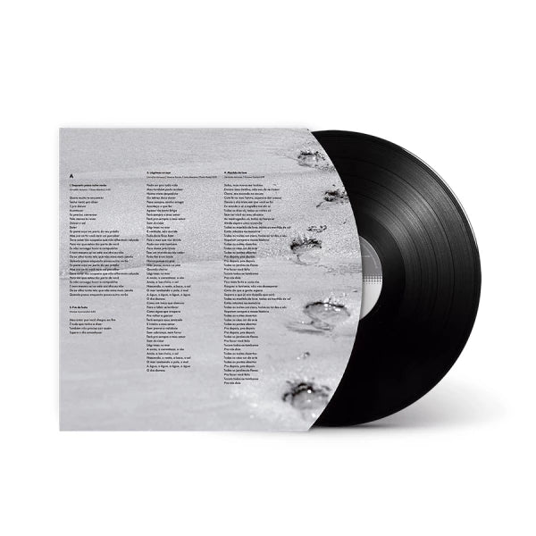 Envelope interno do álbum “Lágrimas no Mar” de Arnaldo Antunes e Vitor Araújo em formato disco de vinil, com letras impressas sobre fotografia em preto e branco de pegadas na areia e disco preto parcialmente exposto (disco de vinil).
