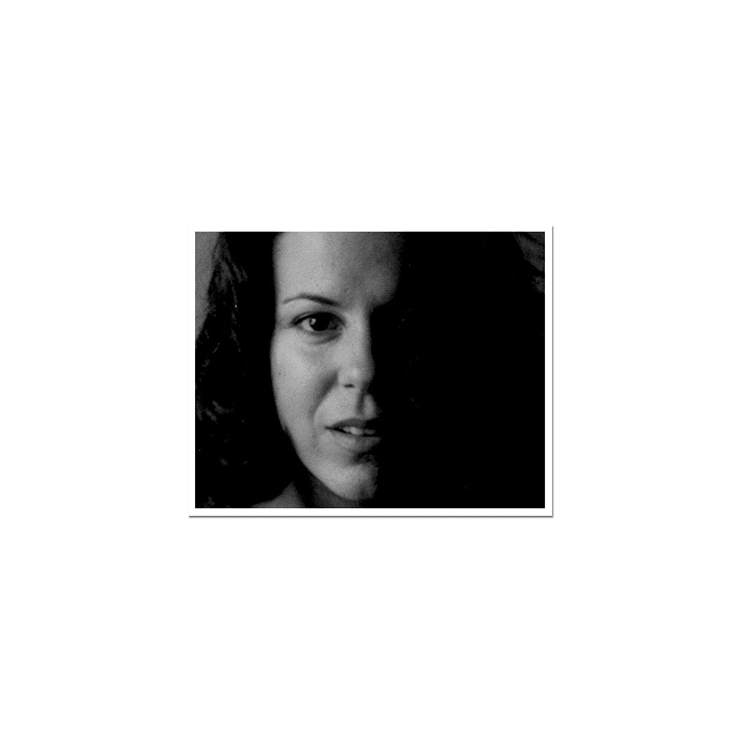 Fotografia artística em preto e branco com forte contraste de luz e sombra, focando em grande plano o rosto de Bebel Gilberto com olhar expressivo.
