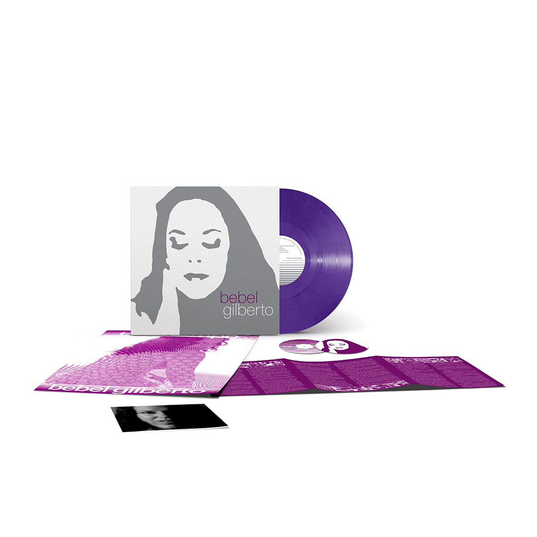 Apresentação da edição especial em vinil do álbum "Tanto Tempo" de Bebel Gilberto. À esquerda, exibe-se a capa cinzenta e branca com o rosto ilustrado. À direita, sobressai o disco de vinil na cor roxa translúcida. À frente, encontram-se dispostos o poster, a revista/encarte desdobrável em tom roxo e uma fotografia impressa da artista.