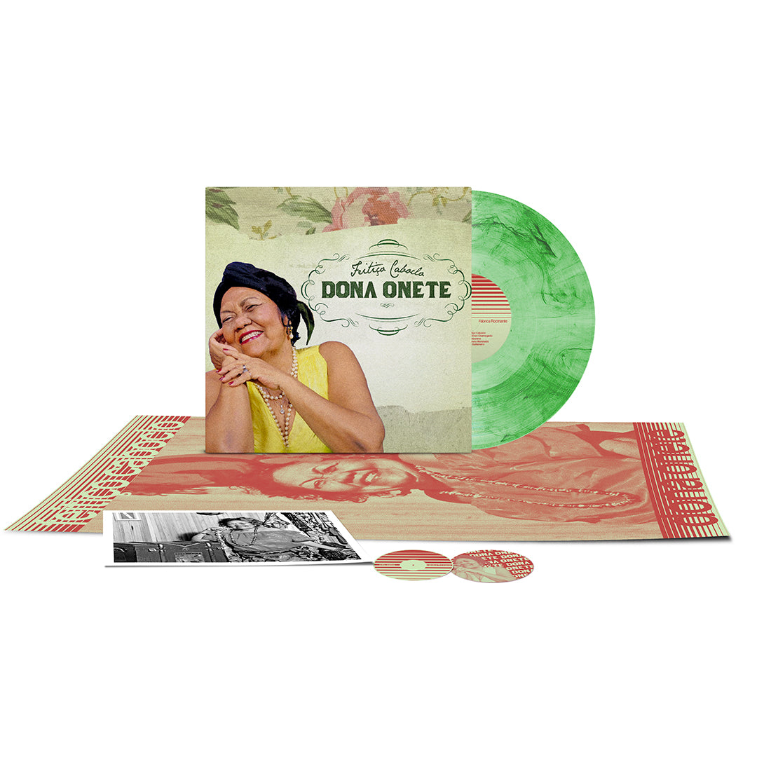 Capa do álbum Feitiço Caboclo de Dona Onete com o disco de vinil parcialmente para fora, tudo sobreposto a um pôster, uma foto A4 e adesivos.