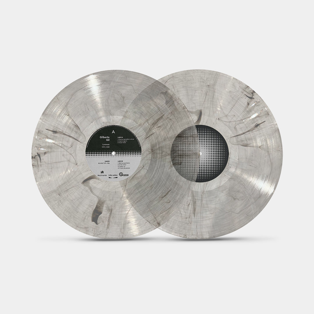Conjunto de dois discos de vinil transparente com efeito fumacê cinza do álbum Luminoso de Gilberto Gil. Os LPs apresentam acabamento translúcido com veios escuros distribuídos pela superfície e selo central com design gráfico em preto e branco.