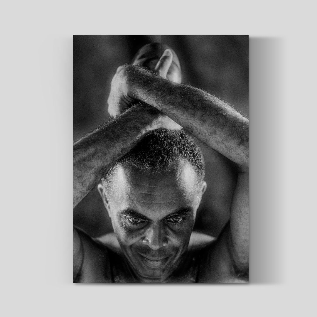 Pôster fotográfico do álbum Luminoso de Gilberto Gil com retrato em preto e branco do artista de braços cruzados acima da cabeça. A imagem possui composição artística e iluminação contrastada, reforçando a estética intimista e contemporânea do projeto.
