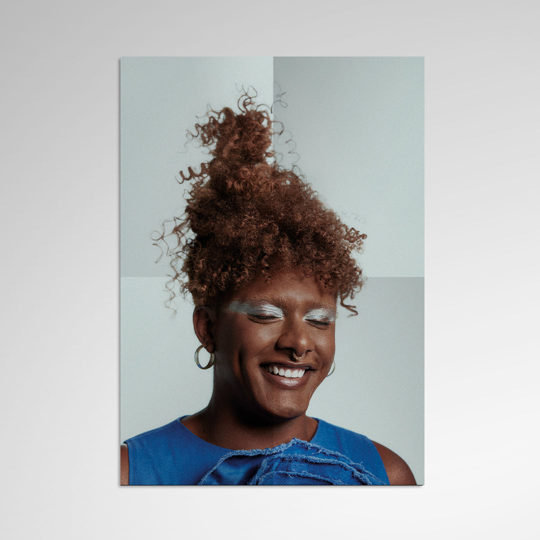 Retrato da artista sorrindo com maquiagem clara nos olhos, brincos de argola e roupa azul sobre fundo neutro (disco de vinil).