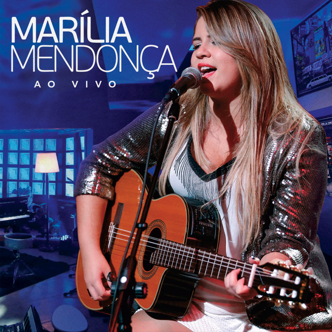 Capa do álbum Ao Vivo, de Marília Mendonça, mostrando a cantora em primeiro plano durante uma apresentação acústica, cantando ao microfone enquanto toca violão. Ao fundo aparece um ambiente de estúdio iluminado por tons de azul, com bateria, piano, escada, luminária e outros equipamentos musicais. O nome da artista e o título do álbum aparecem em destaque no canto superior esquerdo.