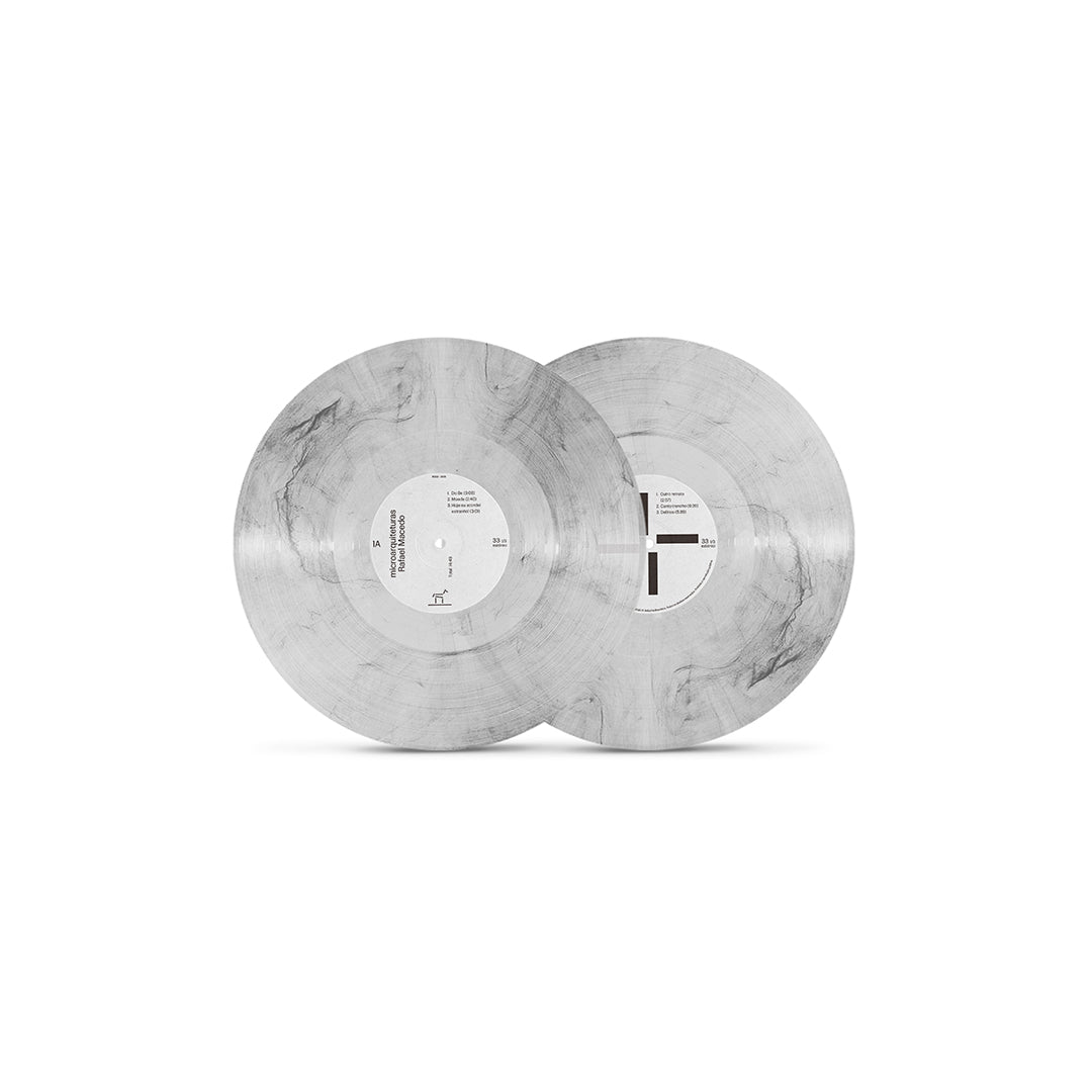 Dois discos de vinil marmorizados em tons de branco translúcido, cinza e veios pretos da edição dupla de Microarquiteturas, com selos centrais brancos de design minimalista e tipografia preta, fotografados parcialmente sobrepostos sobre fundo claro.